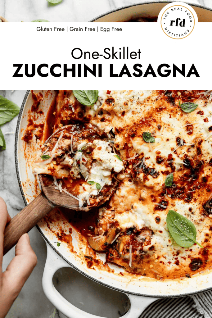 Zucchini lasagna in skillet, wooden spoon scooping up serving 