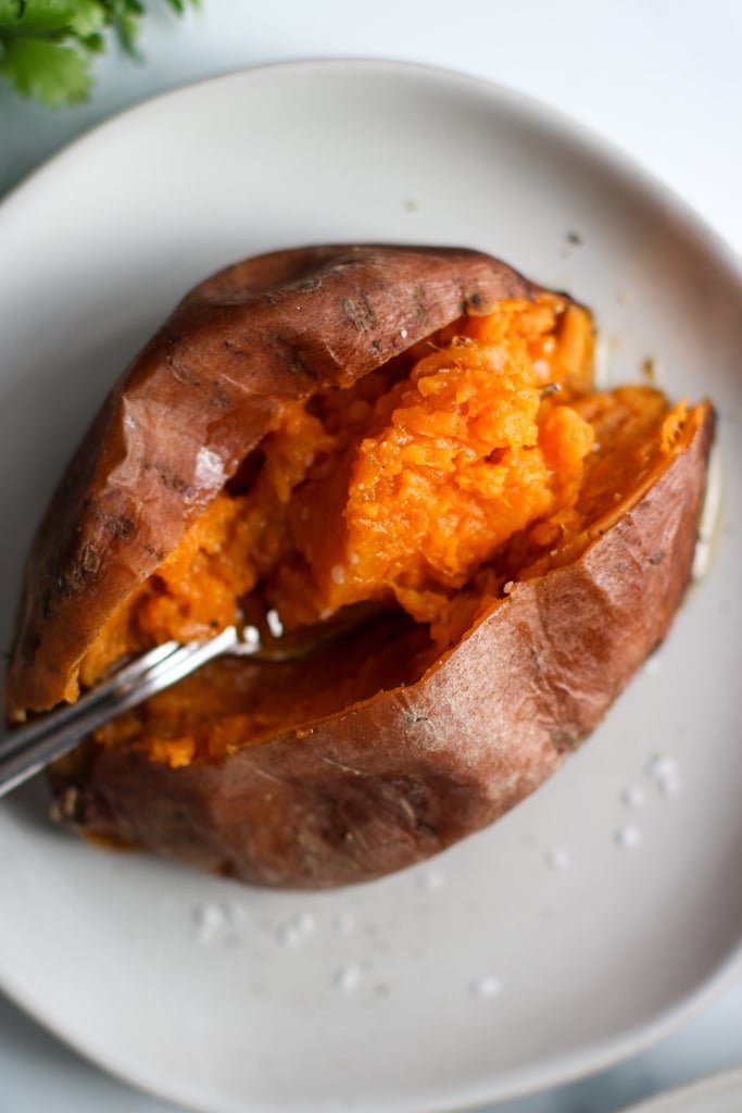 Baked sweet potato cut open with orange fluffy insides on fork