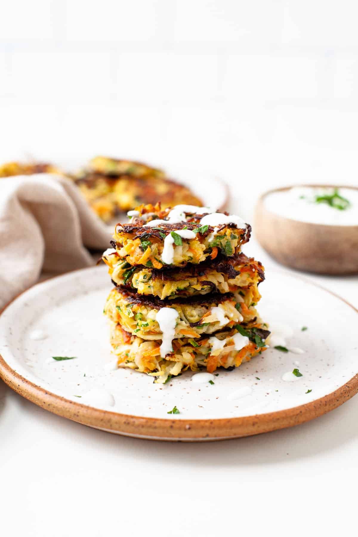 stack of four kohlrabi fritters on speckled plate with herb yogurt sauce drizzled over top