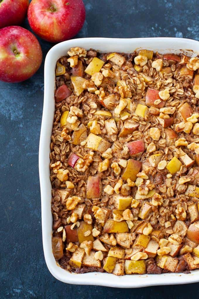 Apple Pie Baked Oatmeal in white baking dish with three apples to the side